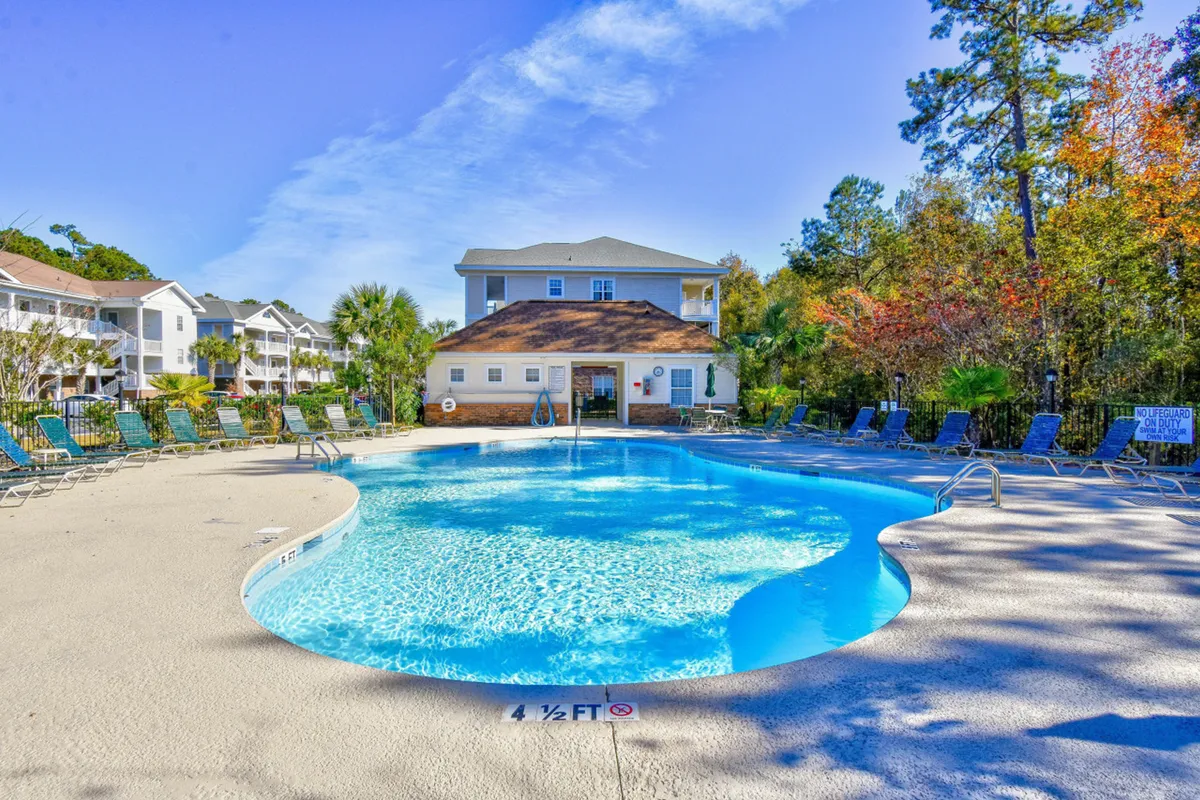 A sparkling community swimming pool surrounded by sun loungers and lush landscaping. The clubhouse in the background and inviting seating highlight the resort-style amenities within easy reach.