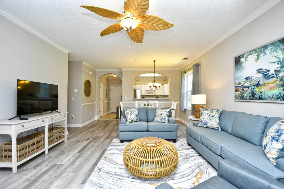 This image portrays a stylish, cozy living room with a large flat-screen TV, woven coffee table, comfortable seating, and colorful artwork—perfect for entertaining, relaxing, or sharing special moments.