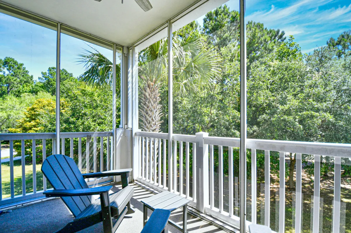 A tranquil screened-in porch with an Adirondack chair and a small side table, overlooking lush greenery. The screened setting allows for enjoying the outdoors while remaining sheltered, and the peaceful view hints at morning coffee or quiet reading.