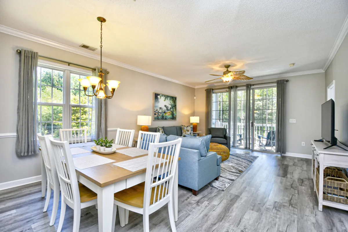 A spacious open-concept living area featuring a comfortable sofa, a dining table set up for family meals, a television for entertainment, and expansive windows that fill the space with natural light. The room is styled with modern decor and plush furnishings, creating a warm, welcoming environment ideal for relaxing or gathering with loved ones.
