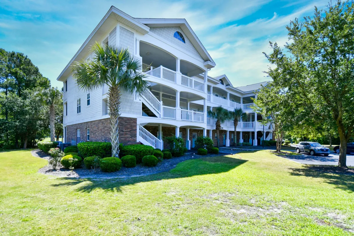 An exterior view featuring palm trees, well-kept green lawn, and balconies set against a backdrop of welcoming architecture. The setting conveys a sense of community, natural beauty, and easy access to outdoor spaces.