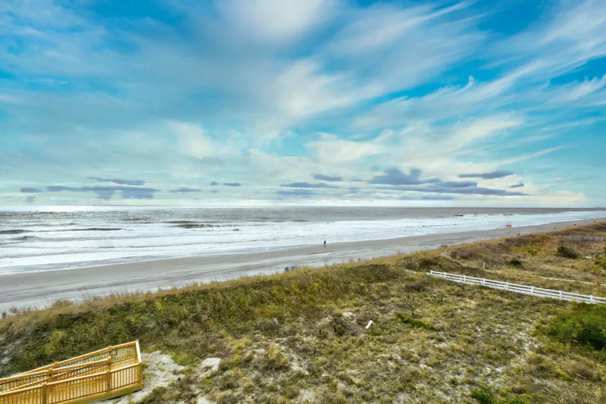 This image captures a tranquil stretch of North Myrtle Beach, featuring soft sandy shores, rolling ocean waves, and a single distant figure walking along the water's edge under a cloud-filled sky. The inviting expanse of the beach is front and center, invoking a sense of relaxation and natural beauty.