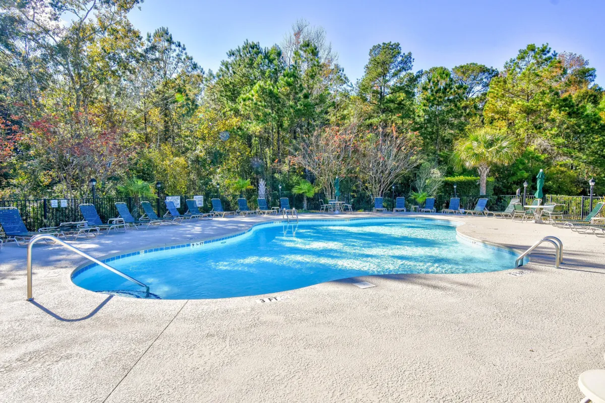 A sparkling swimming pool is surrounded by comfortable lounge chairs and lush greenery, creating a lively and inviting outdoor amenity space. The pool area looks family-friendly and tranquil, ideal for both relaxation and play after a day at the beach.