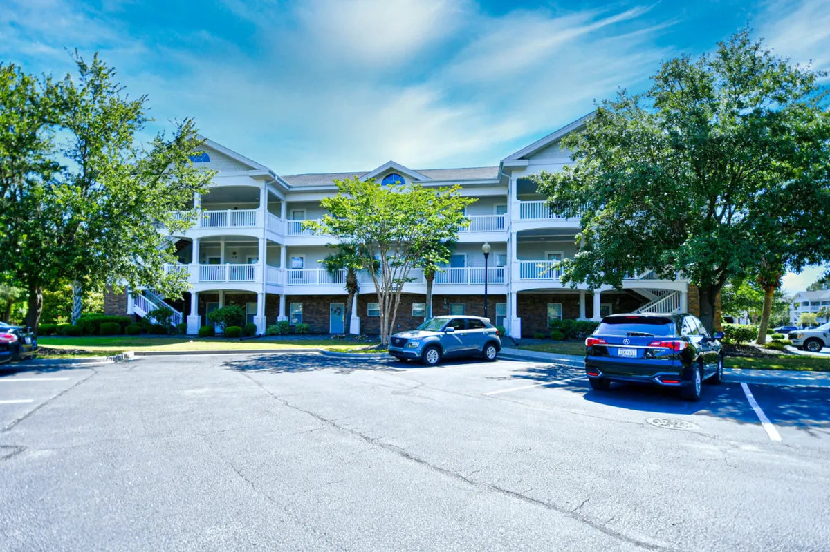 A two-story building framed by green trees and a welcoming parking area, suggesting the comfortable, home-like accommodations within Barefoot Resort.
