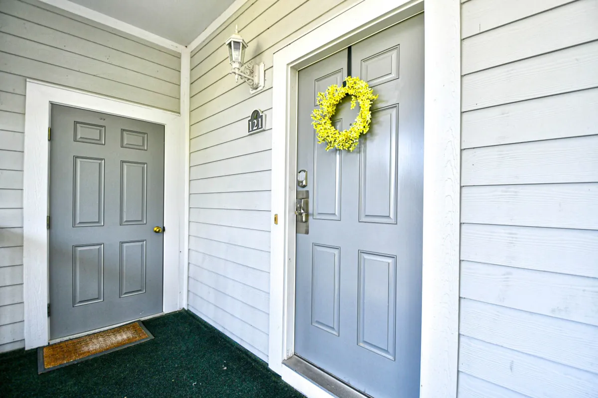 This image captures the inviting exterior entrance of the condo, featuring a gray front door with a cheerful yellow wreath and a secondary entrance door, set against a tidy facade with a lamp fixture. The entryway exudes a welcoming vibe and hints at the comforts within.