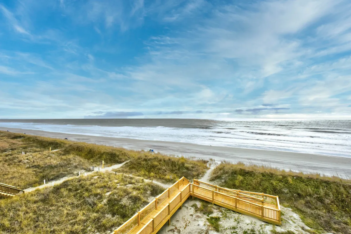 This image captures an expansive beach with rolling waves seen from a wooden deck, evoking the sense of relaxation and scenic beauty available steps away from the condo.